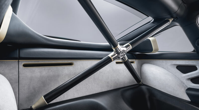 View of the rear interior environment specified with Pebbled Grey leather upper trim. A rear X-brace has been fitted, finished in satin carbon fiber with champagne accents. Behind the X-brace, the carbon fiber ram-air intakes can be seen, directing air to the cooling fan in the engine compartment.